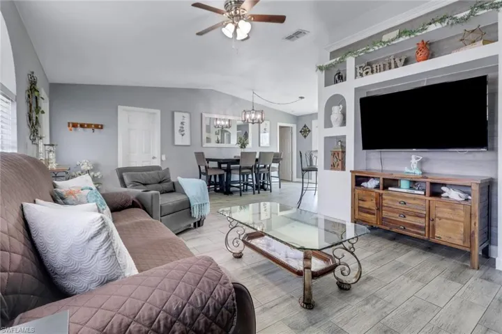 Living room with light wood-type flooring, ceiling fan with notable chandelier, visible vents, and vaulted ceiling