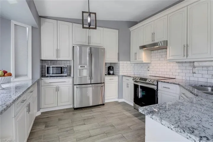 Kitchen featuring under cabinet range hood, light stone counters, white cabinets, and stainless steel appliances