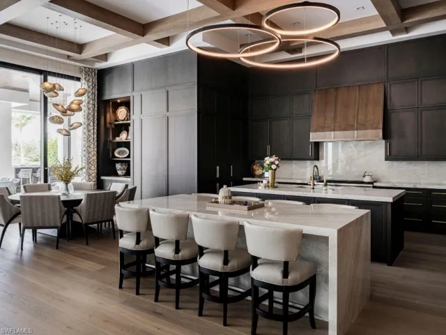 Custom Ruffino cabinetry and millwork in the main kitchen w light stone countertops, a breakfast bar area, and hanging light fixtures