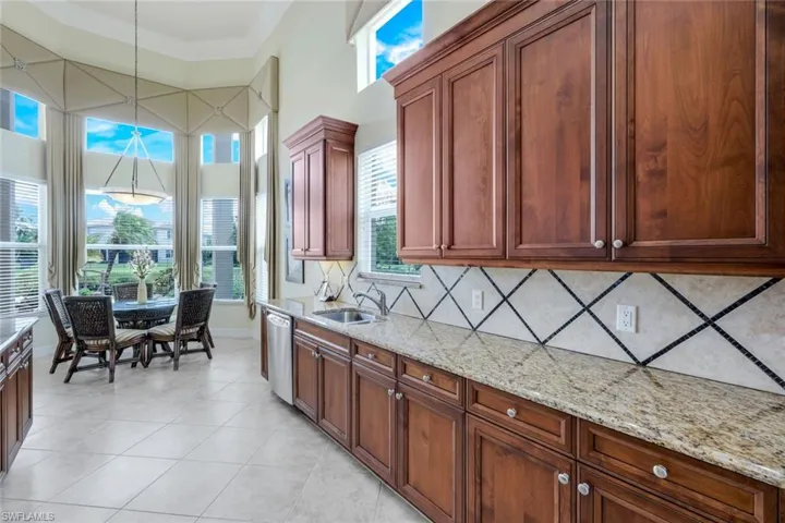 Kitchen with decorative light fixtures, light stone counters, light tile flooring, tasteful backsplash, and stainless steel dishwasher