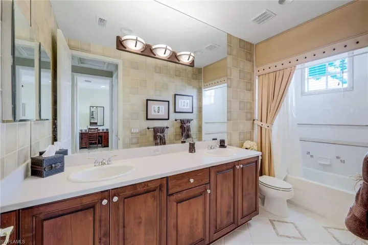 Full bathroom with tile walls, dual sinks, toilet, tile floors, and large vanity