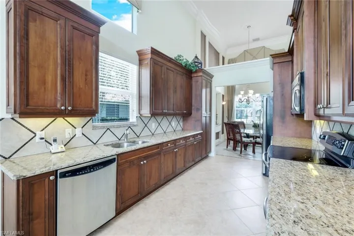 Kitchen featuring backsplash, light stone countertops, appliances with stainless steel finishes, sink, and light tile floors