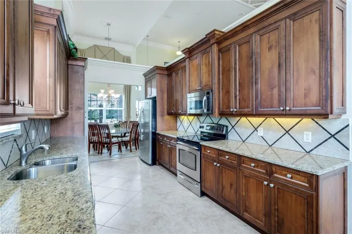 Kitchen with light tile flooring, stainless steel appliances, a notable chandelier, backsplash, and sink