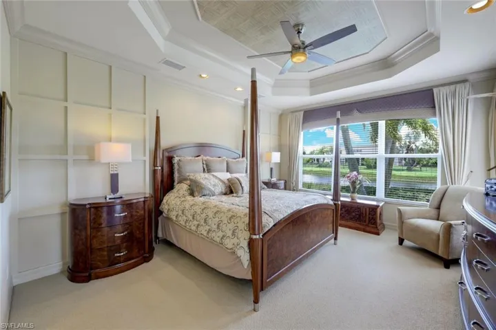 Carpeted bedroom featuring ceiling fan, a tray ceiling, and crown molding