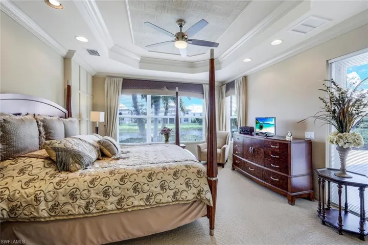 Carpeted bedroom with ornamental molding, ceiling fan, and a raised ceiling