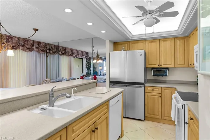 Kitchen with white appliances, recessed lighting, decorative light fixtures, light tile patterned flooring, and a tray ceiling