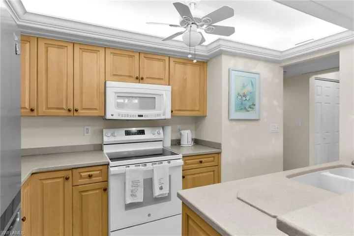 Kitchen featuring white appliances, ceiling fan, light stone countertops, light brown cabinetry, and ornamental molding