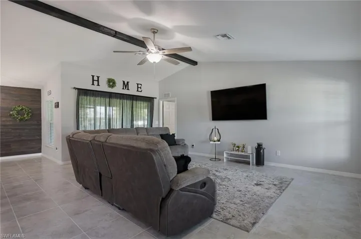 Living room featuring high vaulted ceiling, ceiling fan, beam ceiling, wooden walls, and light tile patterned floors