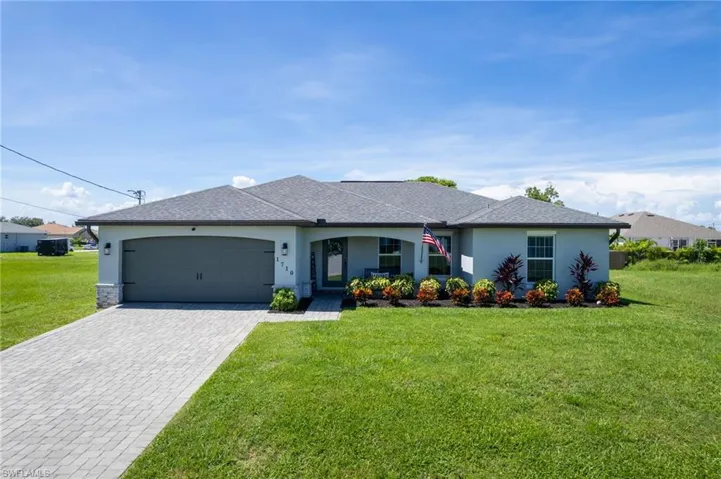 Ranch-style house featuring stucco siding, a front yard, decorative driveway, a shingled roof, and an attached garage