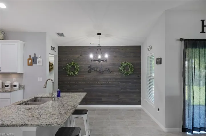 Kitchen featuring wood walls, an accent wall, white cabinets, a kitchen breakfast bar, and light stone counters