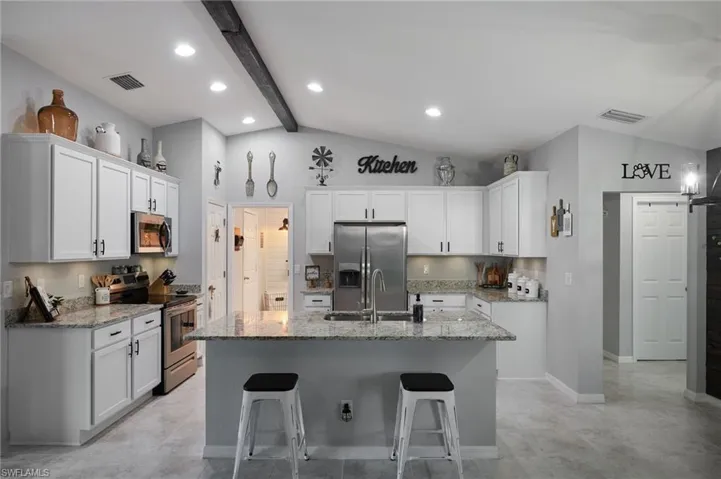 Kitchen featuring appliances with stainless steel finishes, light stone counters, white cabinetry, a breakfast bar, and a kitchen island with sink