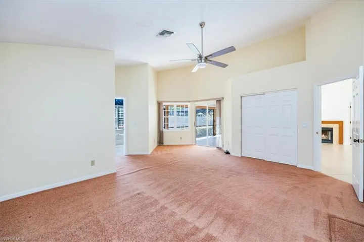Unfurnished living room featuring a tile fireplace, ceiling fan, a towering ceiling, and light colored carpet