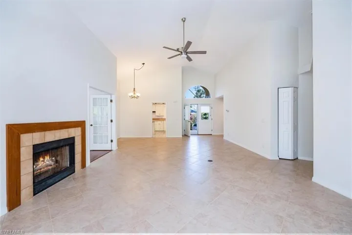 Unfurnished living room featuring a fireplace, light tile patterned floors, ceiling fan with notable chandelier, and high vaulted ceiling