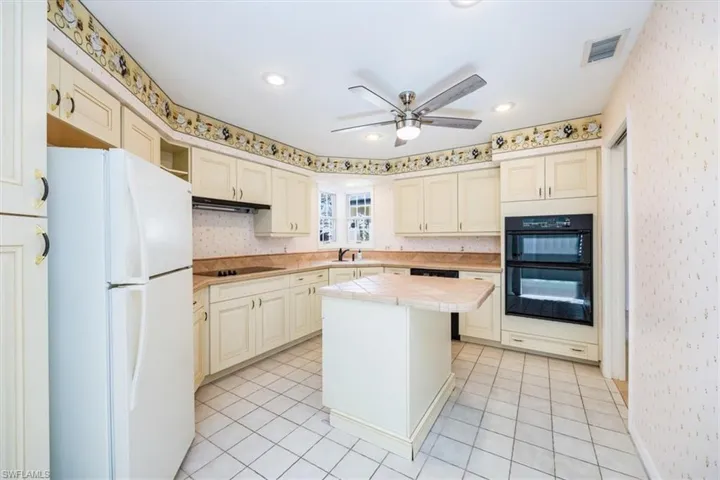 Kitchen featuring ceiling fan, sink, black appliances, tile countertops, and a center island