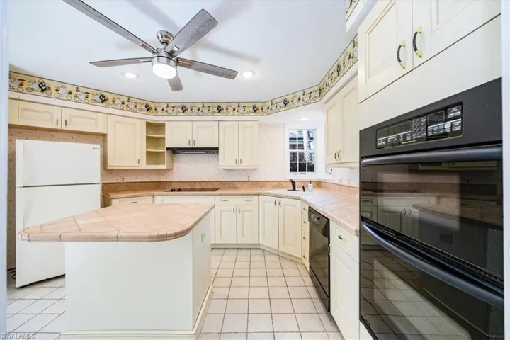 Kitchen with a center island, tile counters, light tile patterned flooring, and black appliances