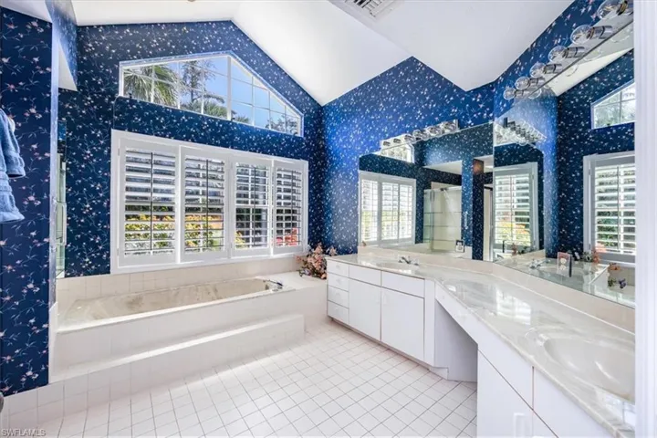 Bathroom with tile patterned flooring, vanity, lofted ceiling, and tiled tub