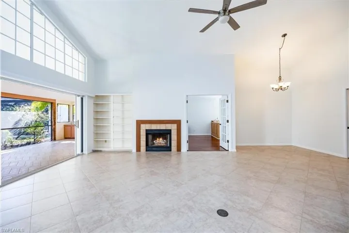Unfurnished living room with a high ceiling, built in features, a tiled fireplace, light tile patterned floors, and ceiling fan with notable chandelier