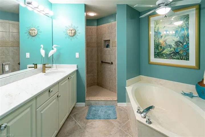 Full bathroom with vanity, a walk in shower, ceiling fan, a garden tub, and light tile patterned flooring