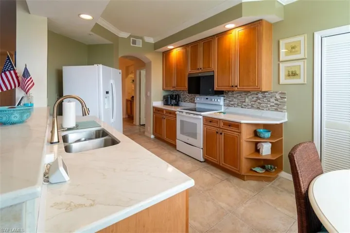 Kitchen with wood finish cabinetry, white appliances, arched walkways, ornamental molding, and light tile patterned flooring