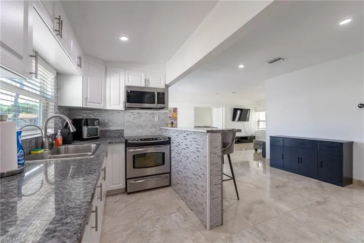 Kitchen with a breakfast bar, appliances with stainless steel finishes, decorative backsplash, dark stone countertops, and white cabinets