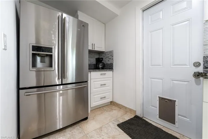 Kitchen with stainless steel refrigerator with ice dispenser, white cabinets, decorative backsplash, dark stone countertops, and light tile patterned floors