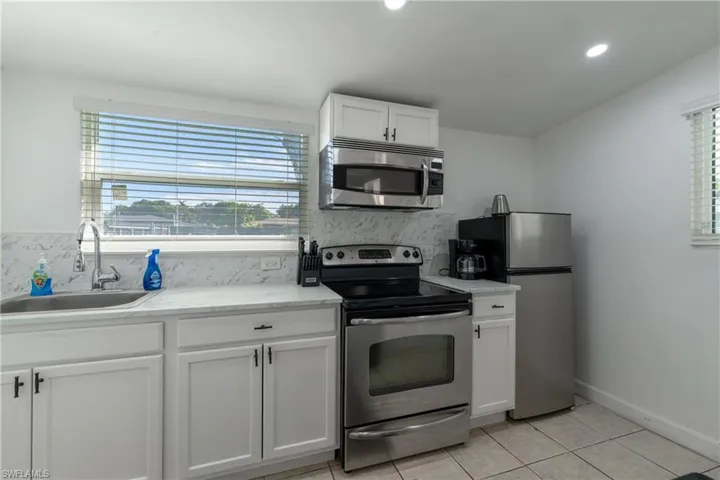 Kitchen with appliances with stainless steel finishes, white cabinets, tasteful backsplash, light tile patterned flooring, and plenty of natural light