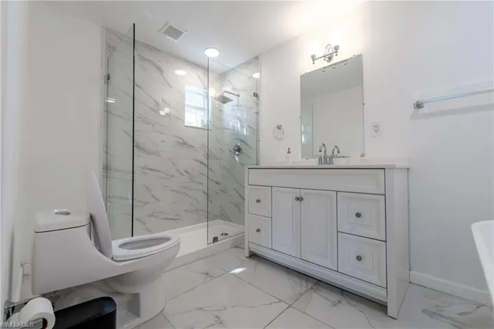 Bathroom featuring light marble finish floors, a marble finish shower, and vanity