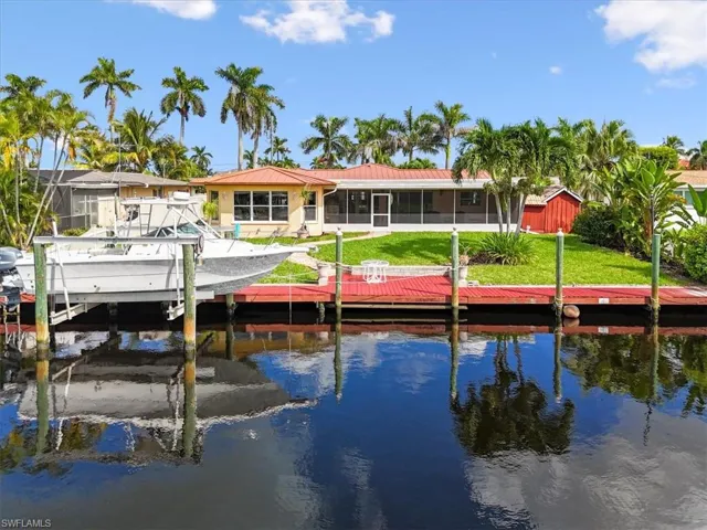 Dock area featuring boat lift, a sunroom, a water view, and a lawn
