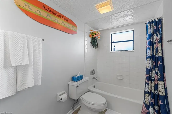 Bathroom with a textured ceiling, shower / bath combo, and toilet