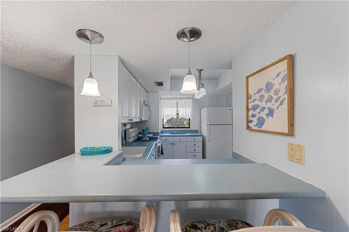 Kitchen featuring pendant lighting, white appliances, kitchen peninsula, and a textured ceiling