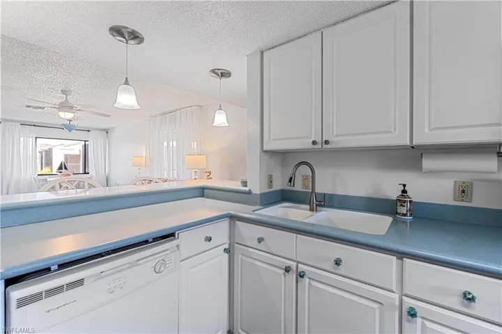 Kitchen with white dishwasher, ceiling fan, white cabinets, and sink