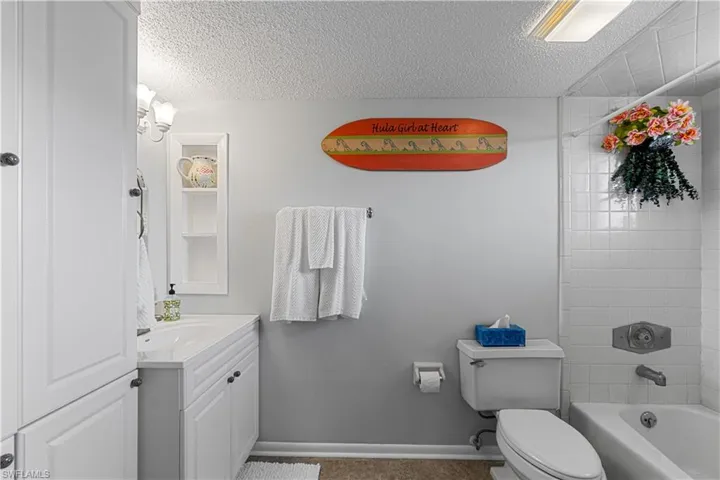 Full bathroom with a textured ceiling, vanity, toilet, and tiled shower / bath combo