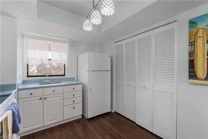 Kitchen with a textured ceiling, dark wood-type flooring, white refrigerator, white cabinets, and hanging light fixtures
