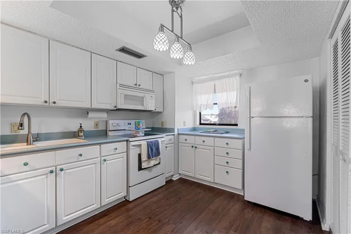 Kitchen with pendant lighting, white appliances, white cabinets, sink, and dark hardwood / wood-style flooring