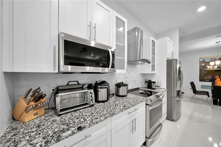 Kitchen with white cabinetry, wall chimney range hood, and appliances with stainless steel finishes