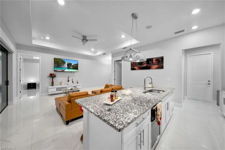 Kitchen featuring sink, a tray ceiling, white cabinets, a center island with sink, and decorative light fixtures