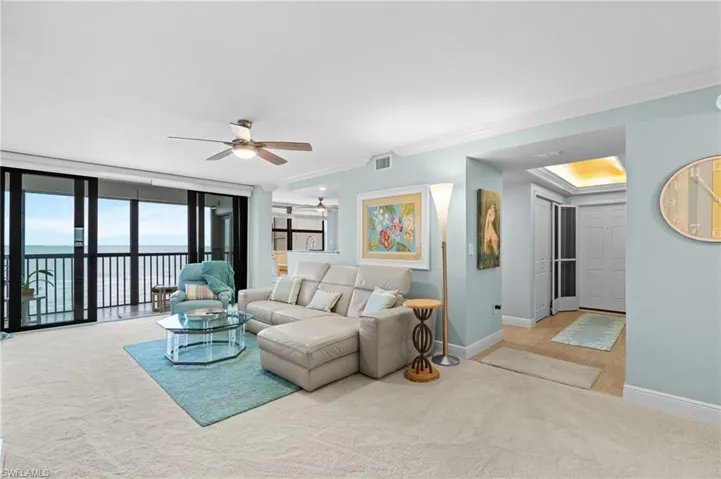 Living area with ceiling fan, ornamental molding, light carpet, expansive windows, and a water view