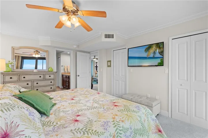 Bedroom featuring two closets, crown molding, light colored carpet, ceiling fan, and connected bathroom