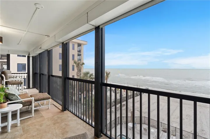 Balcony featuring view of water and beach and a sunroom