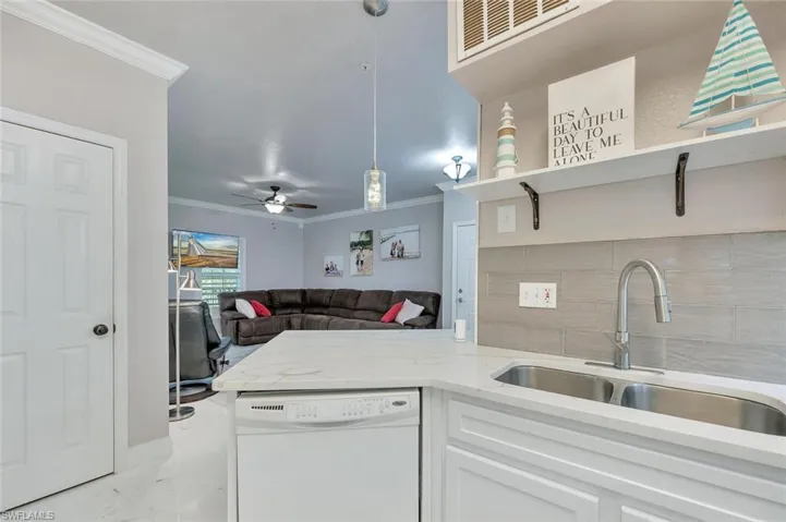 Kitchen with white dishwasher, white cabinets, light stone countertops, open shelves, and crown molding