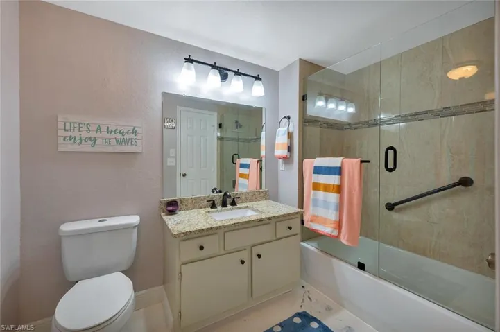 Bathroom with shower / bath combination with glass door, vanity, and a textured wall