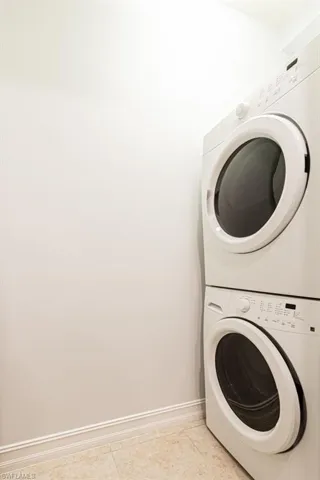 Laundry area with stacked washer and clothes dryer and light tile patterned flooring