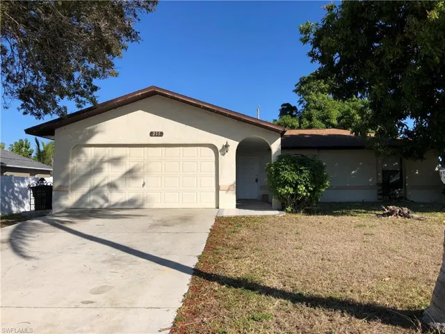 Ranch-style house with driveway, an attached garage, a front yard, and stucco siding