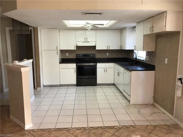 Kitchen featuring dark countertops, black range with electric cooktop, light tile patterned floors, decorative backsplash, and white dishwasher
