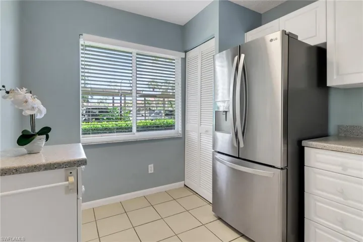 Kitchen with white cabinets, stainless steel fridge, light tile patterned floors, and light stone counters