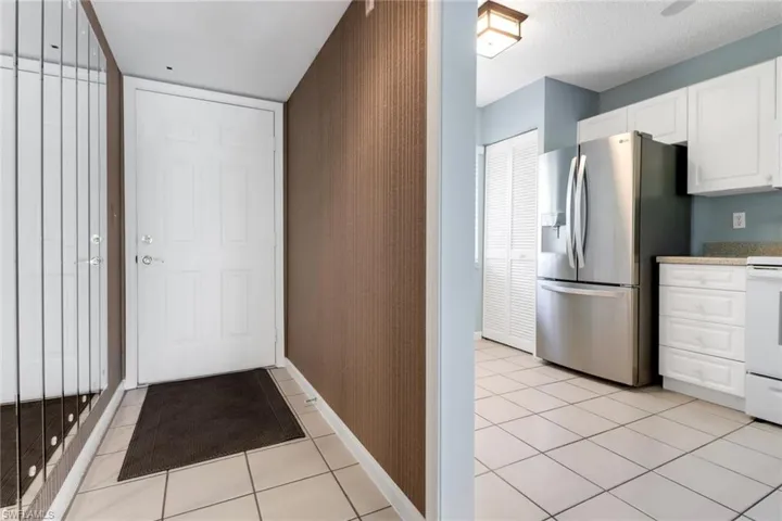 Kitchen with stainless steel refrigerator with ice dispenser, white cabinets, white range oven, light tile patterned flooring, and light stone countertops