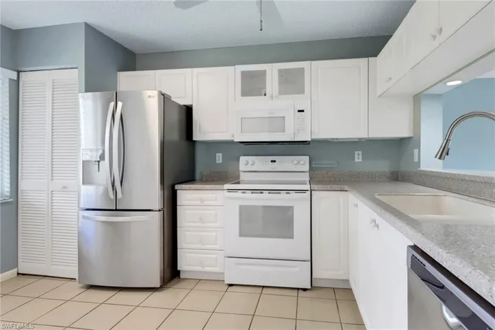 Kitchen featuring stainless steel appliances, glass fronted cabinets, white cabinetry, light tile patterned floors, and a textured ceiling