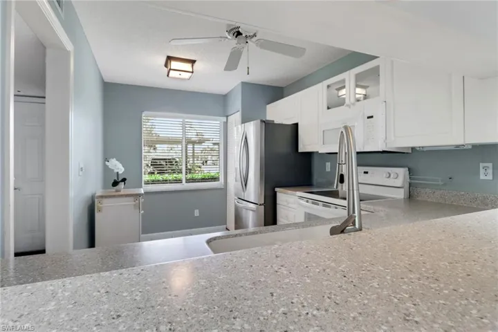 Kitchen featuring white cabinets, glass fronted cabinets, light stone counters, a ceiling fan, and white appliances