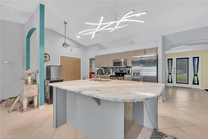 Kitchen featuring vaulted ceiling, stainless steel appliances, gray cabinets, light stone countertops, and a kitchen island with sink
