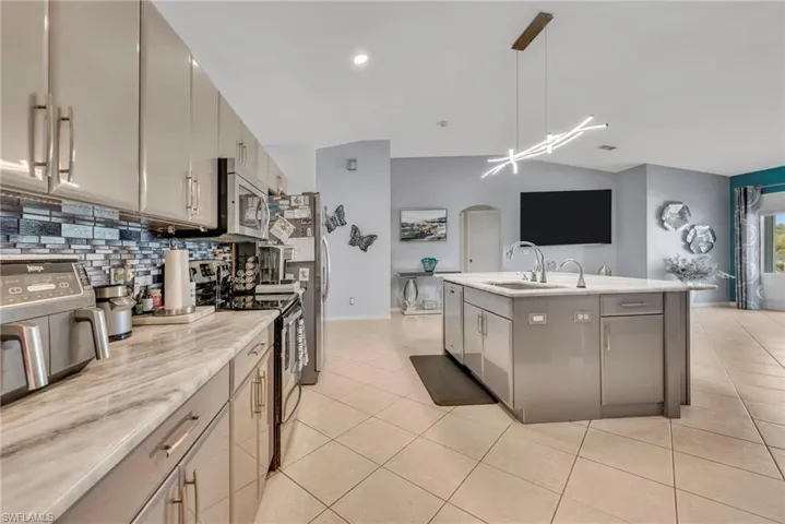 Kitchen with stainless steel appliances, an island with sink, light tile patterned floors, hanging light fixtures, and lofted ceiling